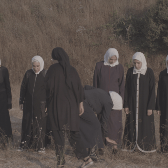 Still from Q. Seven women wearing hijabs in a field.