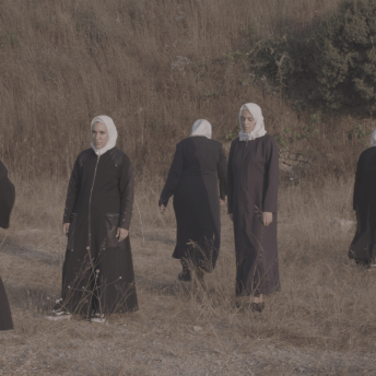 Still from Q. Seven women wearing hijabs walk around in a field.