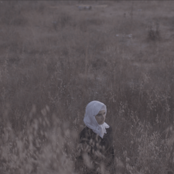 Still from Q. A woman wearing a hijab is walking through a field.