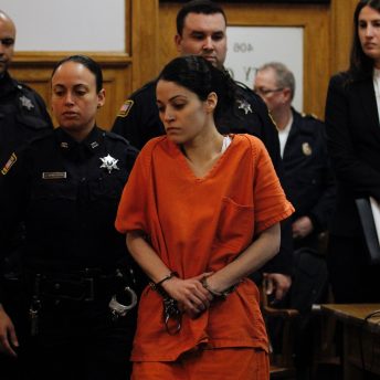 Still from And So I Stayed. A woman is wearing an orange prison uniform, she is handcuffed and is walking in front of several police officers.