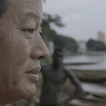 Luan's side face is featured, with Thomas, topless, standing in the background, blurred.