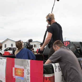 A production crew is in the back of a truck that has posters with the name Ashley and Leonard