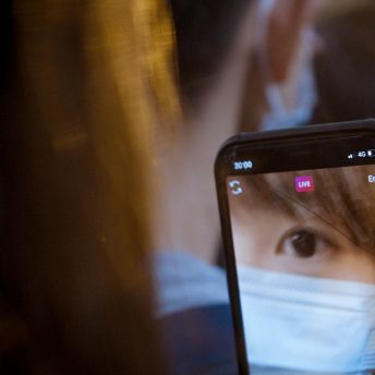 Close up to the screen of a cellphone where we can see the eye of a woman wearing a facemask