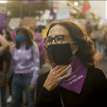 A woman wearing a face mask and a handkerchief knot to her neck, she is in a demonstration