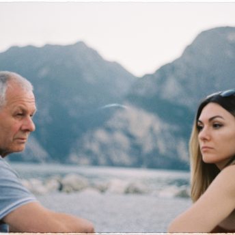 Lina and her father are sitting on a bench next to each other, looking in different directions.