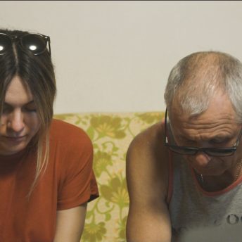 A woman and a man sat in a couch and look down