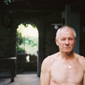 Medium shot of a man standing in front of the camera, shirtless and out of focus