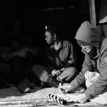 A crew member writes on a clapperboard, in the back there are actors