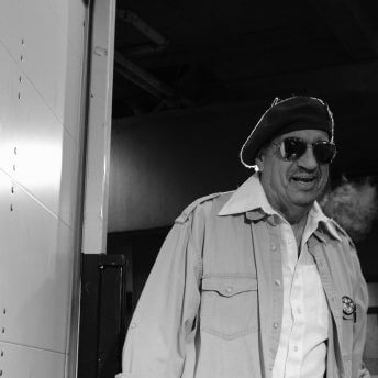 Low angle shot of an actor, wearing a shirt, a jacket, a beret, and dark glasses