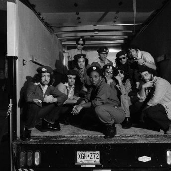 A group of actors dressed as members of the Young Lords Party inside of the back of a trailer truck, looking at the camera