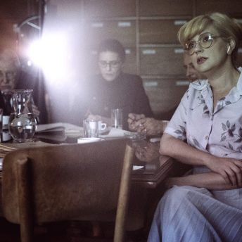 Still from Chuck Norris vs Communism. Irina Nistor and the national television censorship committee watch a film. They all sit facing the camera. Behind them, there is a beam of light shining from the film projector. (photographer Balla Zoltán)