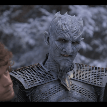 Still from Game Of Thrones: The Last Watch A man wearing prosthetics makeup and armor looks quizzically at an actor and director, both white, wearing dark clothes standing in front of him. He is dressed as the villainous character The Knight King, but his expression is kind.