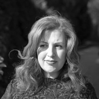 Jeanie Finlay looks away from the camera in profile and smiles. She is wearing a green leopard print dress and has shoulder-length, wavy ginger hair. Black and white portrait.