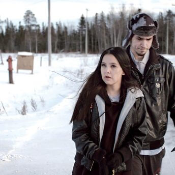 Still from Indictment: The Crimes of Shelly Chartier. Shelly Chartier and her husband Rob Marku walk down a snowy rural road with tense looks on their faces. Shelly is looking away from the camera to her left and Rob is looking downwards.