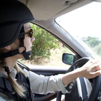 Production still of Displaced. Olha Zhurba, director of Displaced, is in a side profile to the camera. She is driving a car while wearing a helmet and sunglasses.