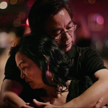 Middle aged Asian man wearing glasses embraces middle aged Asian woman.