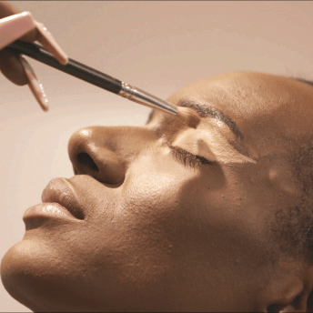 Still from MnM. Close up to the face of a person while a hand is using a brush to paint their eyelids.