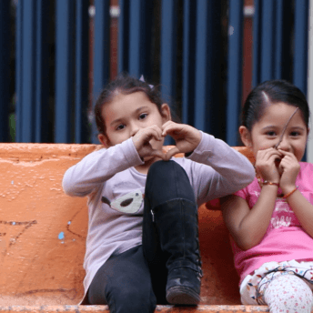 Two five-year-old girls enjoy their time together sitting on a park bench.