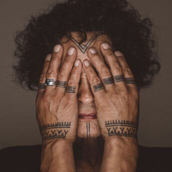 The main character of Twice Colonized, Aaju Peter, in a close-up shot holding her hands in front of her face so her traditional tattoos on her hands and her chin are visible.