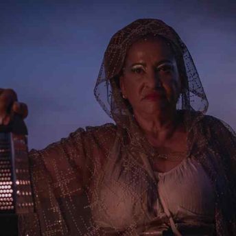 Idaliz with a silver cape holds a lantern as she walks through the night sky.