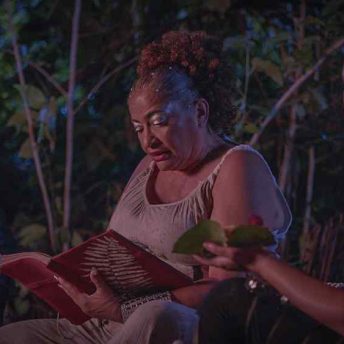 Idaliz with her hair pulled back reads from a red book with a silver plated leaf on the cover.