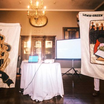one banner, reading 'Lewis' at the top, is held next to a second banner, reading 'Lewis Green Reunion', both with embroidered designs on the front