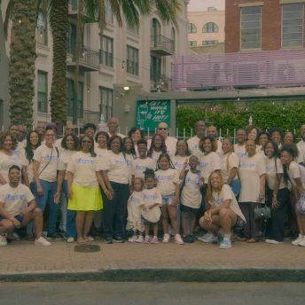 a group of Black people of various skin types smile for a family photo underneath a palm tree