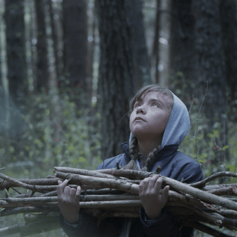 A little girl gathers sticks in the woods and looks up at the sky.